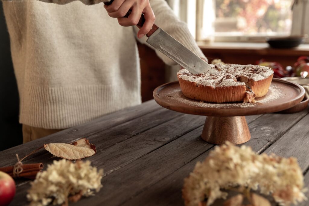 Personne découpant un gâteau fraîchement cuit sur un support en bois, créant une ambiance chaleureuse et cocooning d'automne à l'intérieur.