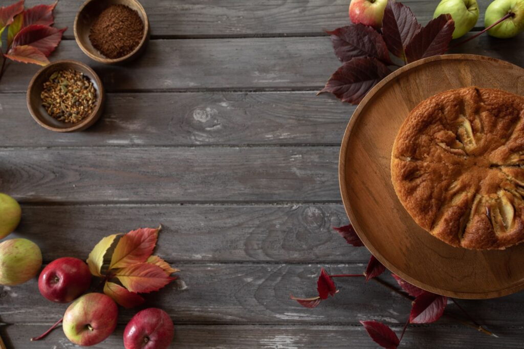 Vue de dessus d'un gâteau aux pommes rustique avec des épices et des feuilles sur une table en bois.