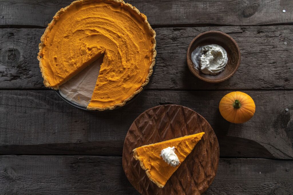 Vue de dessus d'une tarte à la citrouille sur du bois rustique avec de la crème fouettée et une petite citrouille.