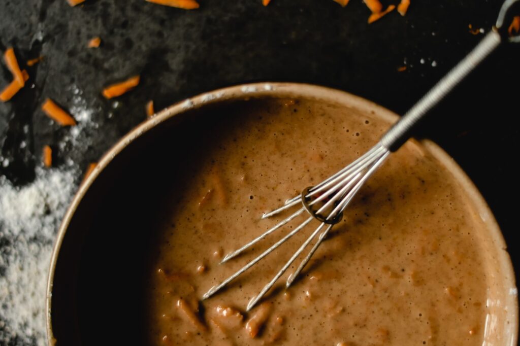 Un bol de pâte à gâteau aux carottes avec un fouet, mettant en valeur les ingrédients de pâtisserie et la préparation.