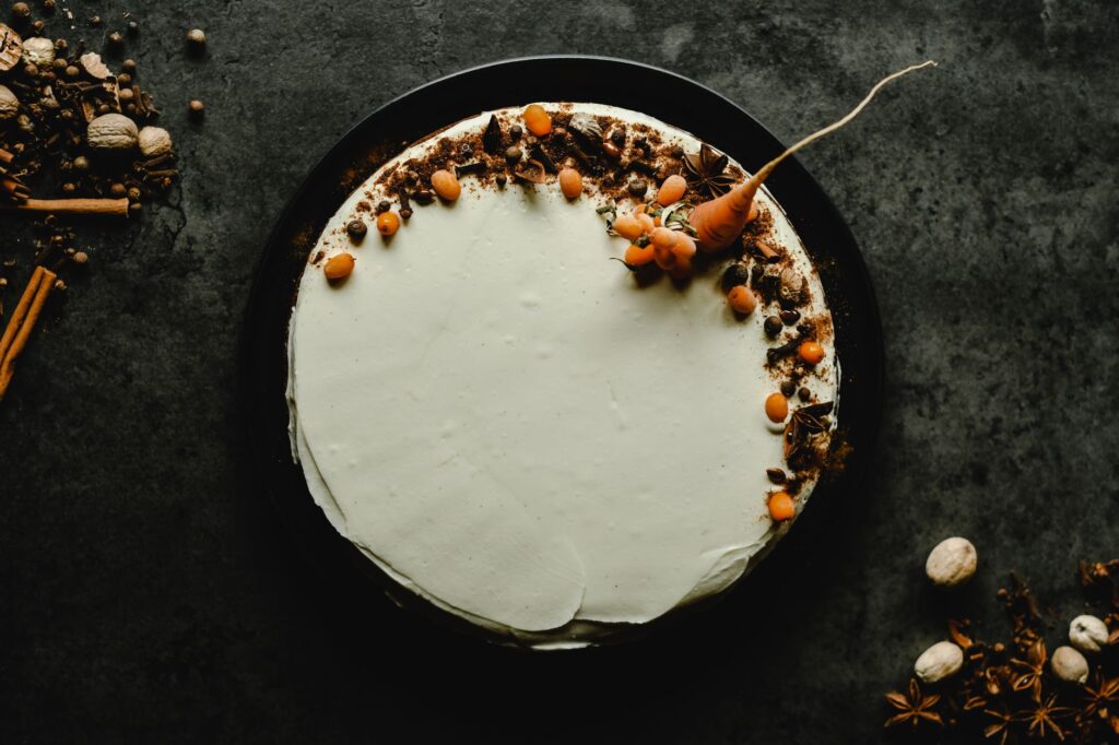 Vue de dessus d'un gâteau aux carottes avec un glaçage au fromage à la crème garni d'épices sur un fond texturé sombre.