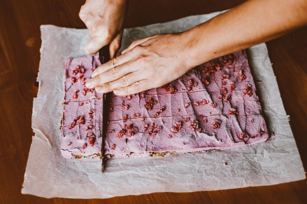 Vue de dessus d'une femme coupant un gâteau aux framboises fait maison sur du papier sulfurisé.