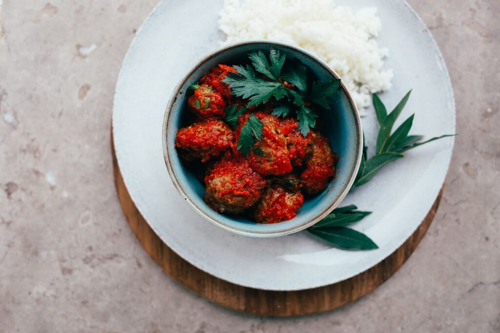 Vue de dessus de boulettes de viande dans une sauce tomate servies avec du riz, garnies d'herbes fraîches.