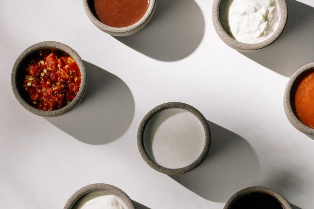Vue du dessus de bols avec diverses sauces et dips projetant des ombres sur une surface blanche.