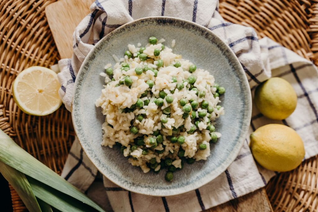 Délicieux risotto garni de petits pois, servi avec des citrons frais sur un décor en osier rustique.