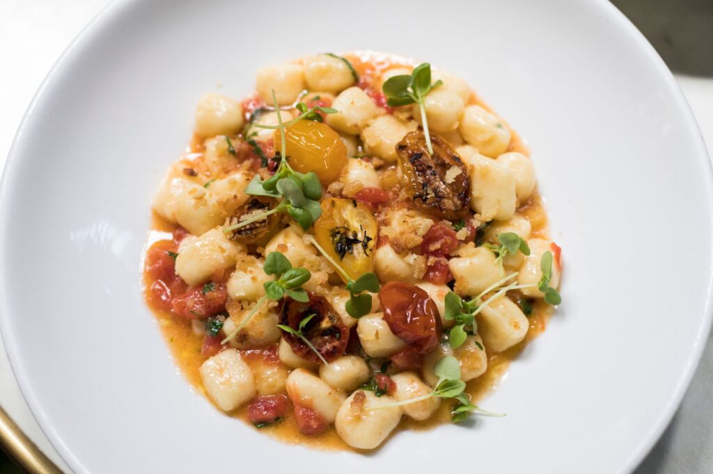 Vue de dessus de gnocchis faits maison avec des tomates fraîches et des herbes sur une assiette blanche.