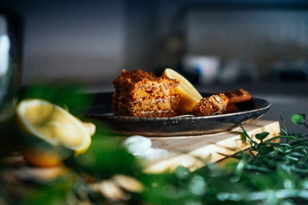 Gros plan d'une part de gâteau au citron sur une assiette avec des ingrédients frais, mettant en valeur la lumière naturelle et la texture.