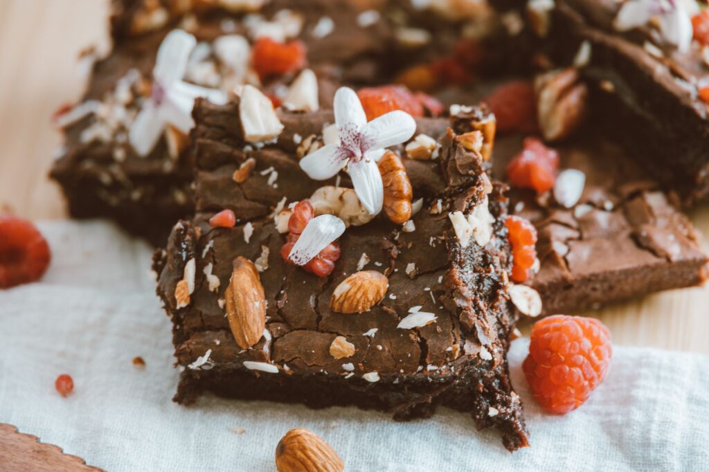 Gros plan de brownies faits maison garnis d'amandes et de framboises, mettant en valeur des décorations florales pour une touche artistique.