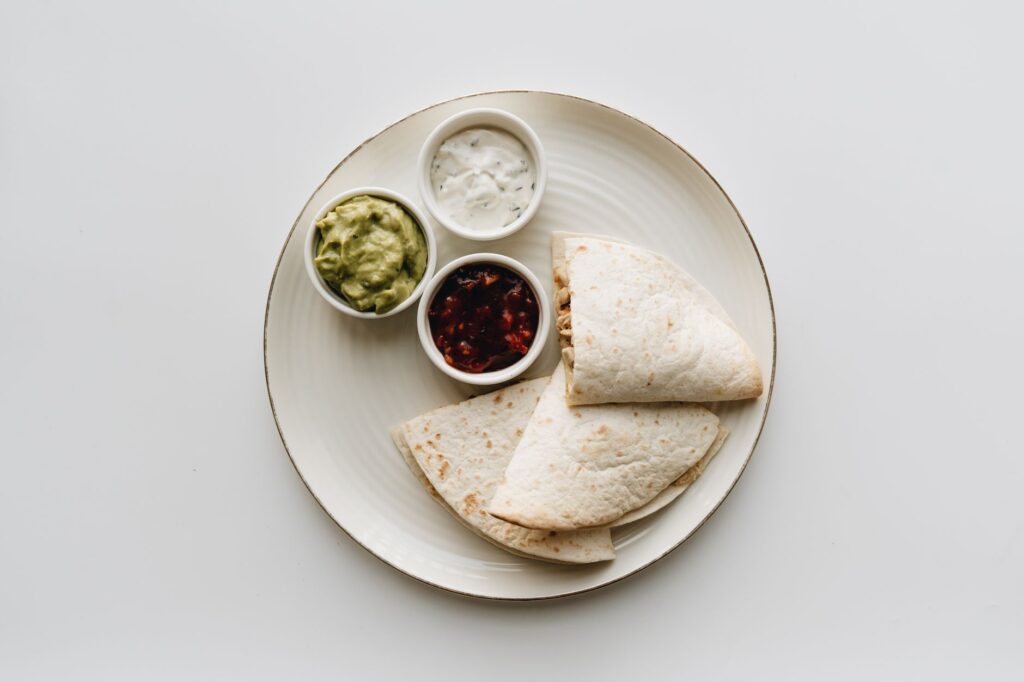 Vue de dessus d'une quesadilla mexicaine servie avec du guacamole, de la salsa et de la crème aigre sur une assiette.