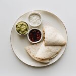 Vue de dessus d'une quesadilla mexicaine servie avec du guacamole, de la salsa et de la crème aigre sur une assiette.
