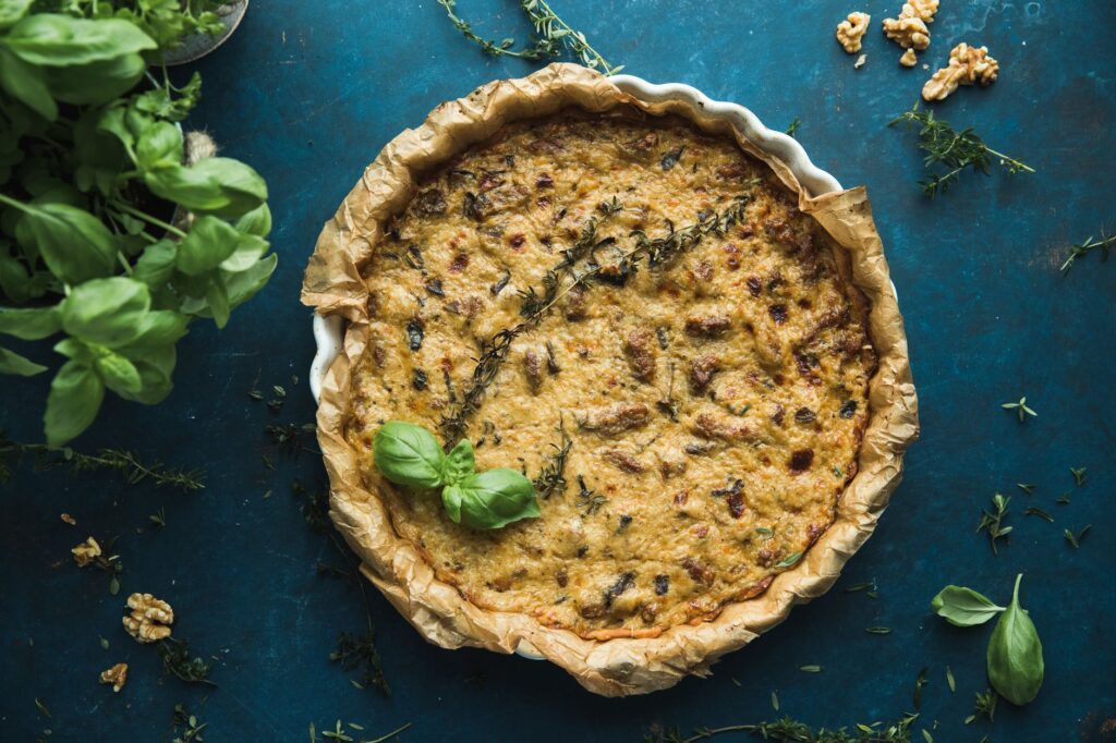 Délicieuse quiche maison avec des herbes fraîches sur une surface bleue rustique, parfaite pour des présentations culinaires.