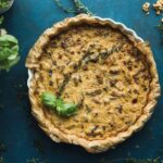 Délicieuse quiche maison avec des herbes fraîches sur une surface bleue rustique, parfaite pour des présentations culinaires.