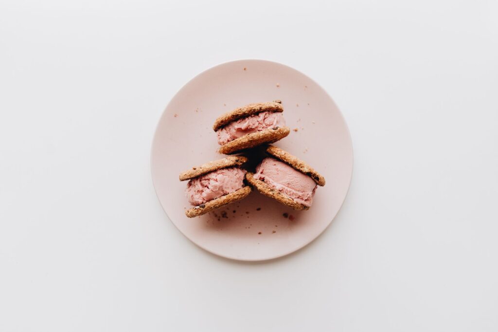 Trois sandwichs à la crème glacée sur une assiette rose, parfaits pour l'été.