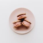 Trois sandwichs à la crème glacée sur une assiette rose, parfaits pour l'été.
