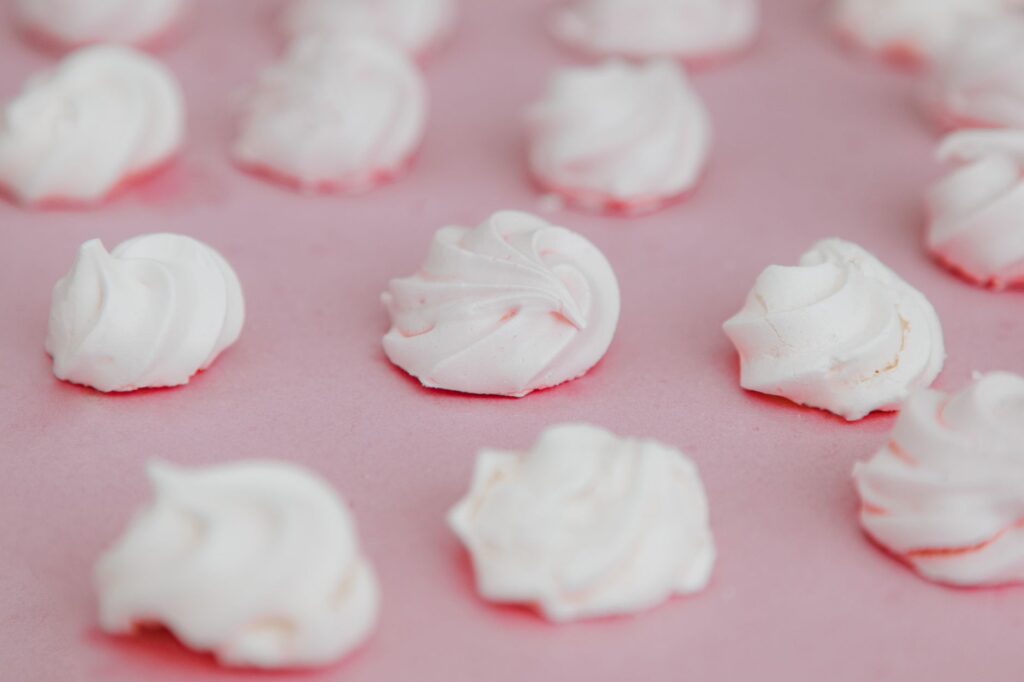 Des biscuits meringués blancs élégamment présentés sur un fond rose doux, mettant en valeur leur texture délicate.