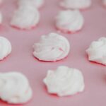 Des biscuits meringués blancs élégamment présentés sur un fond rose doux, mettant en valeur leur texture délicate.
