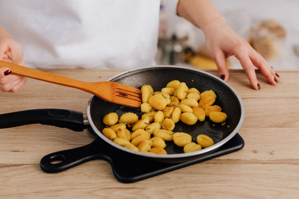 Gros plan sur la cuisson des gnocchis dans une poêle avec une spatule en bois sur une table en bois.