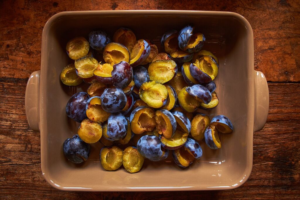 Vue de dessus de prunes juteuses tranchées dans un plat de cuisson rustique sur une table en bois, parfait pour la cuisson ou la cuisine.