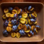 Vue de dessus de prunes juteuses tranchées dans un plat de cuisson rustique sur une table en bois, parfait pour la cuisson ou la cuisine.