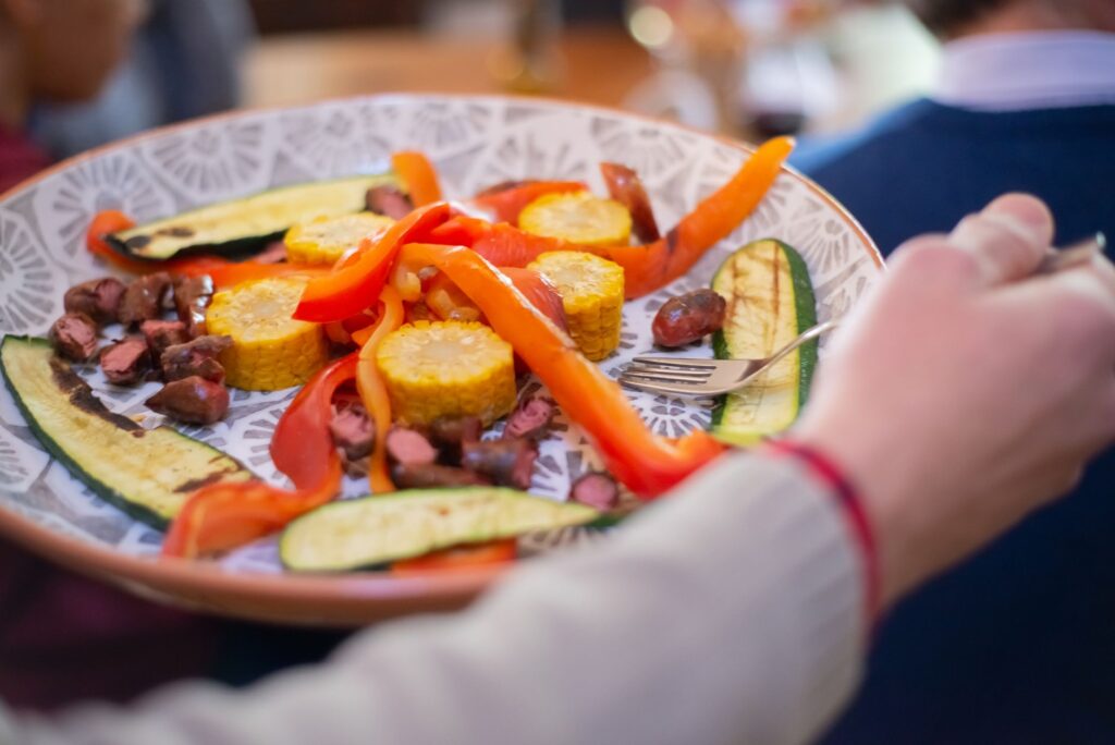 Légumes grillés colorés incluant des courgettes, du maïs et des poivrons rouges sur une assiette décorative.