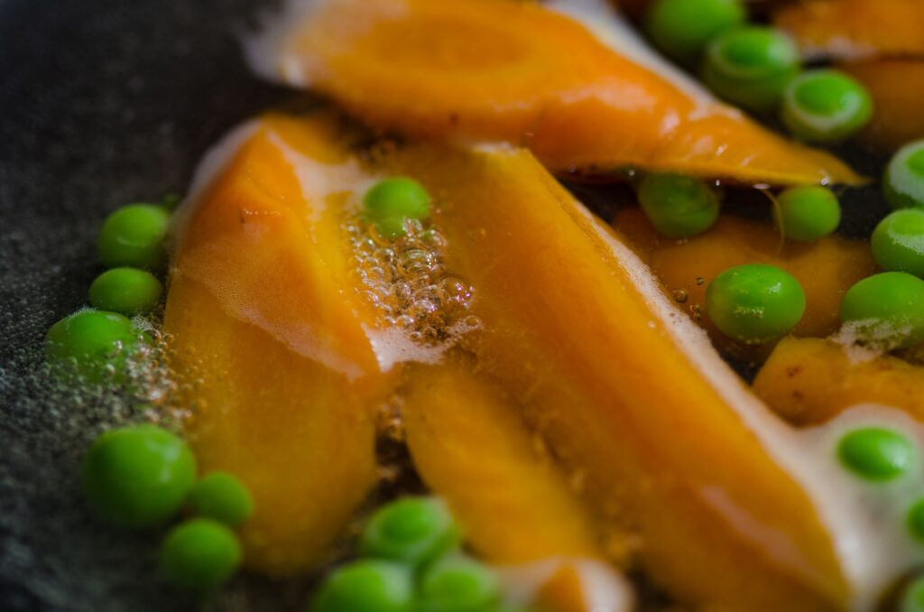 Gros plan de carottes et de pois bouillant avec des bulles dans de l'eau chaude, mettant en valeur des légumes frais.