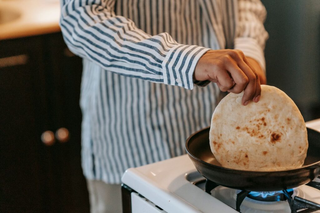 Gros plan d'une personne cuisinant du pain plat sur une cuisinière, mettant en avant la cuisine maison décontractée.