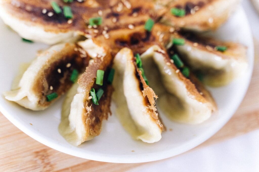 Délicieux dumplings croustillants poêlés, garnis d'oignons verts et de graines de sésame, sur une assiette blanche.