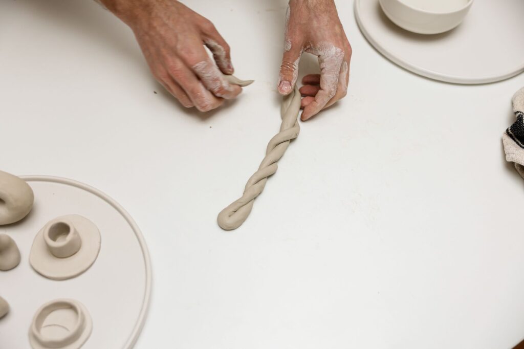 Mains façonnant de l'argile pour créer des porte-bougies, mettant en valeur l'artisanat fait main sur une surface blanche propre.