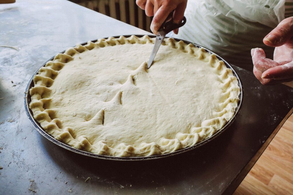 Mains habiles taillant une croûte de tarte maison avec des ciseaux dans une cuisine.
