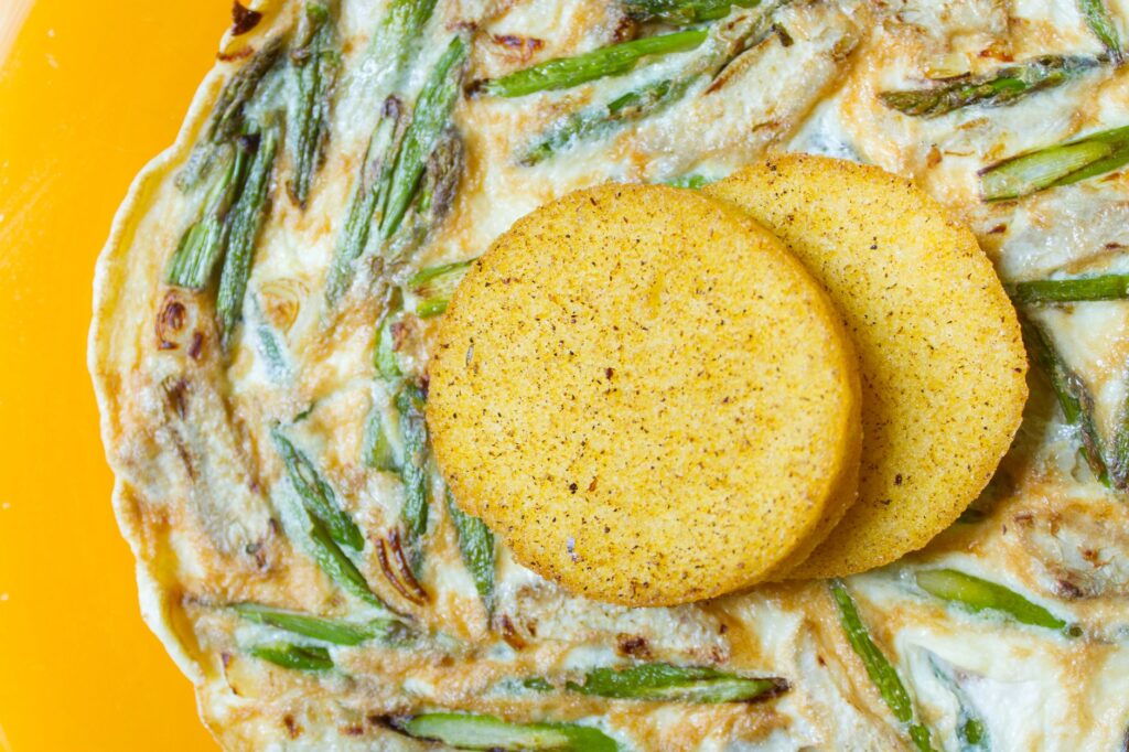 Gros plan sur des arepas servies avec une omelette aux asperges sur une assiette brillante.