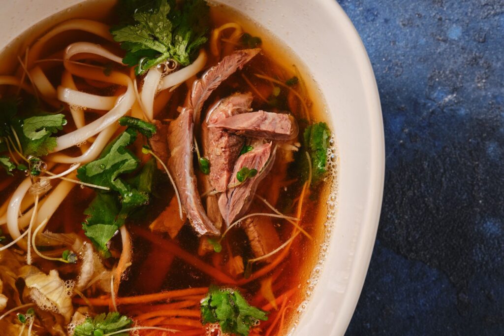 Délicieuse soupe de nouilles au bœuf asiatique garnie d'herbes fraîches, capturée en gros plan sur un fond bleu.