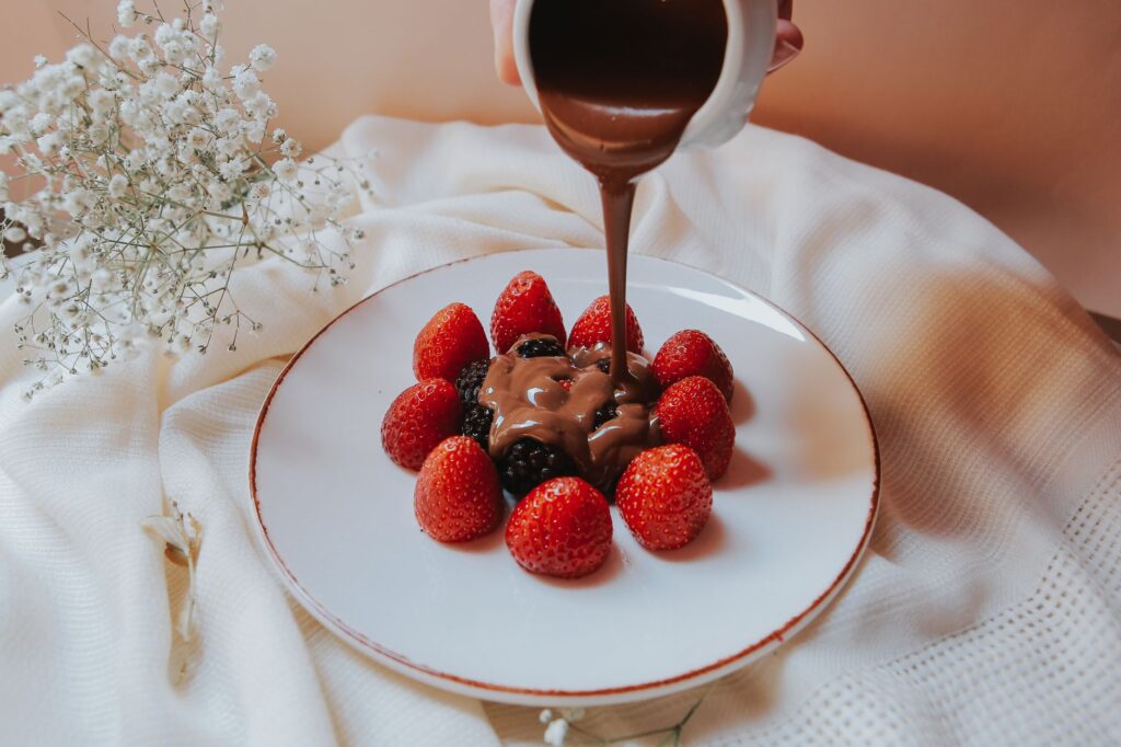 Sauce au chocolat élégamment versée sur des fraises fraîches et des mûres dans une assiette en porcelaine.