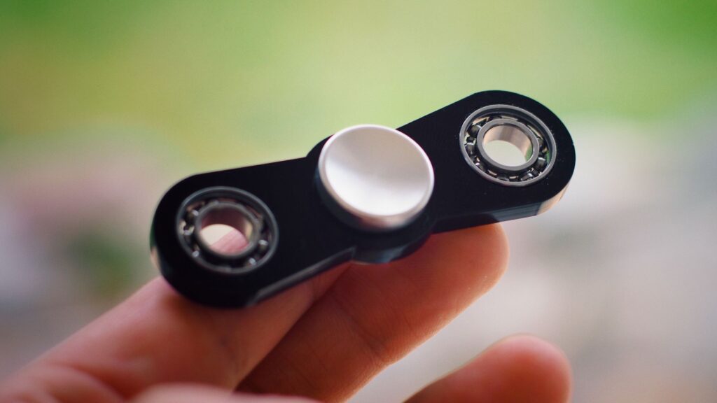 Vue en gros plan d'un spinner fidget noir tenu entre des doigts avec un arrière-plan flou.