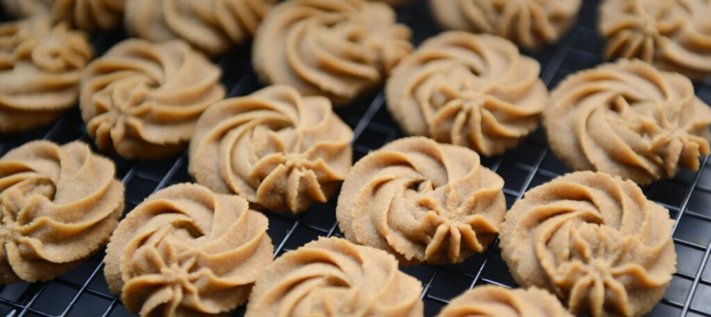 Des biscuits au beurre fraîchement cuits disposés sur une grille de refroidissement, mettant en valeur leurs tourbillons complexes.