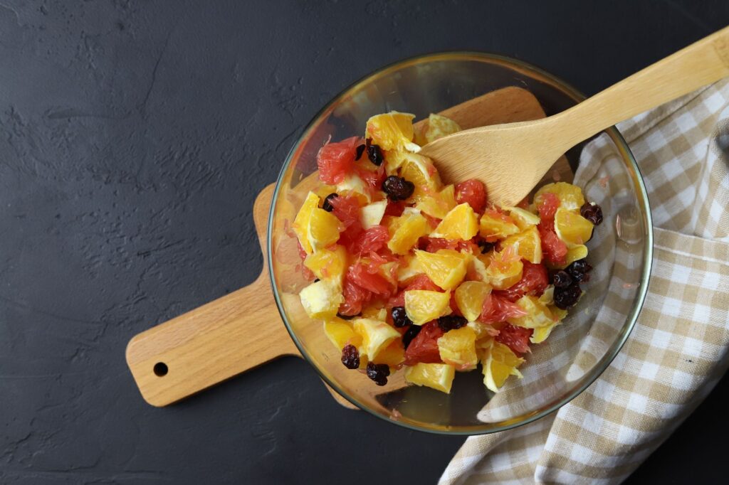 Salade de fruits colorée avec des agrumes et des baies servie dans un bol en verre sur une planche en bois.