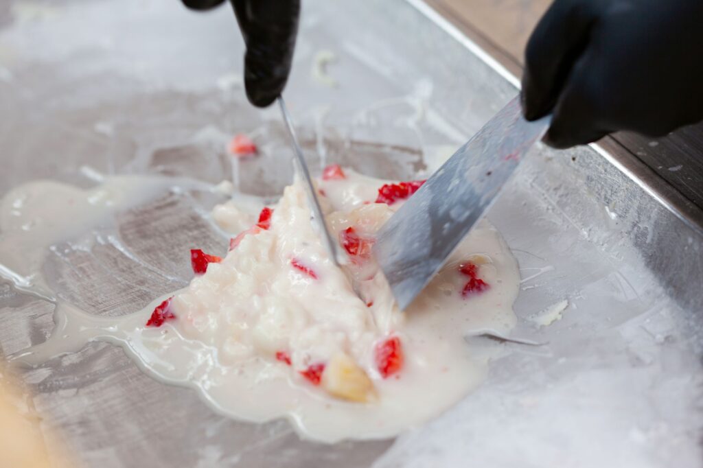 Gros plan sur la fabrication de glace roulée fraîche avec des fraises sur une plaque froide.