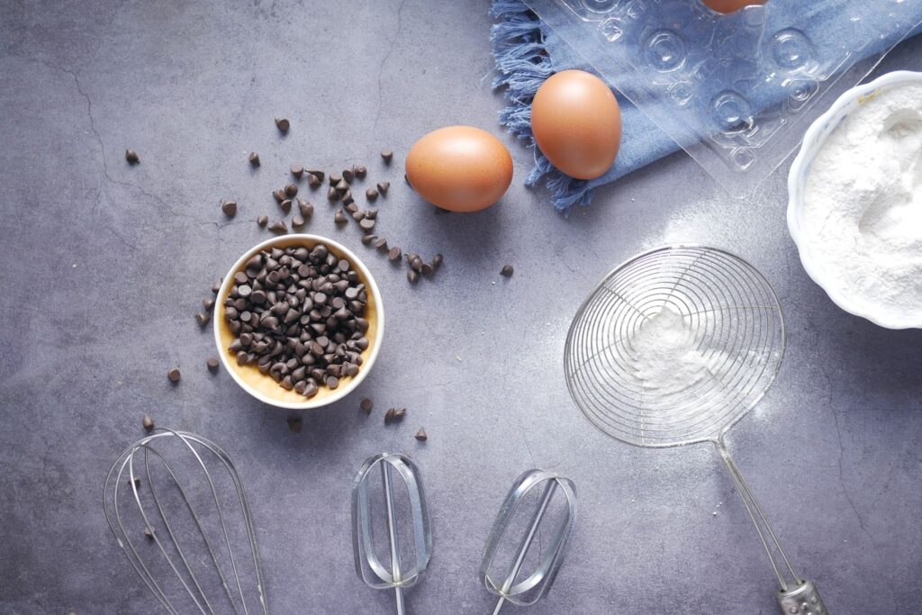Vue de dessus des essentiels de pâtisserie avec des pépites de chocolat, des œufs et de la farine sur un plan de travail.