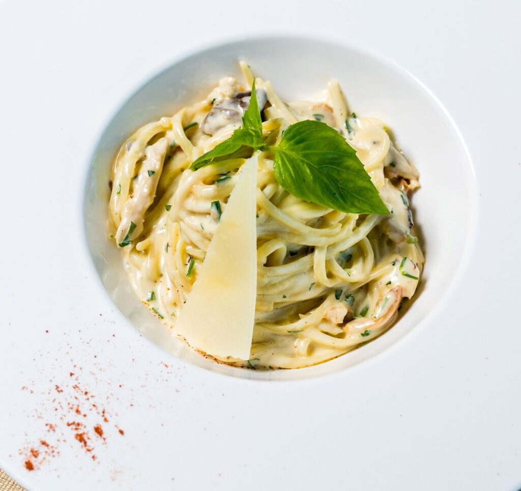 Délicieux plat de spaghetti crémeux garni de basilic et de parmesan dans un bol en céramique.