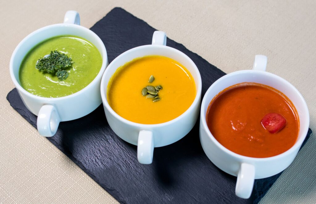 Une variété de soupes végétariennes présentées dans des mugs blancs, avec des saveurs de brocoli, de citrouille et de tomate.