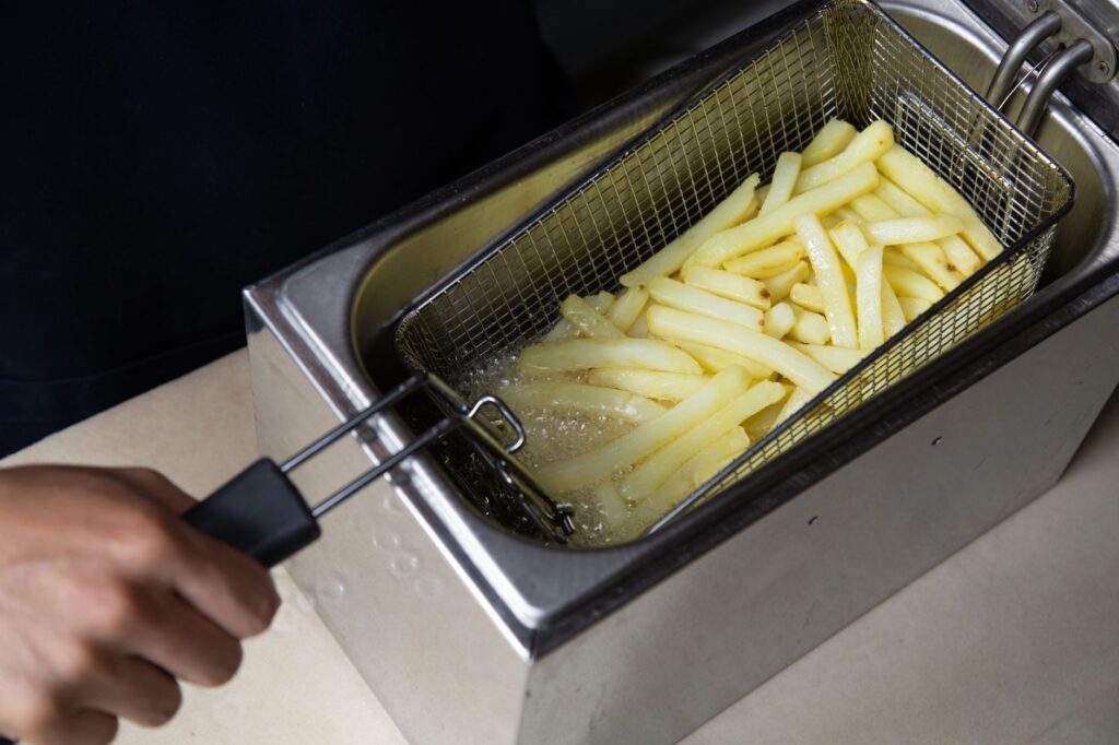 Gros plan sur des frites en train d'être frites dans une friteuse commerciale, main tenant le panier.