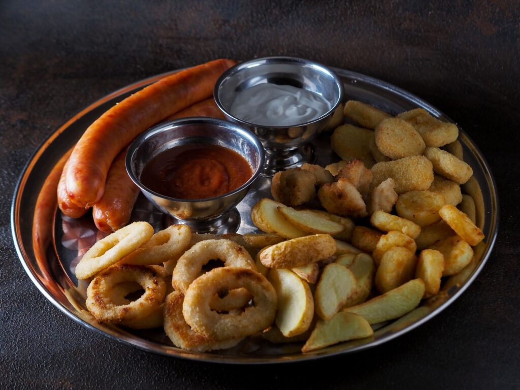 Délicieux plateau de saucisses, frites et dips servi sur une assiette en acier inoxydable.