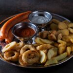 Délicieux plateau de saucisses, frites et dips servi sur une assiette en acier inoxydable.
