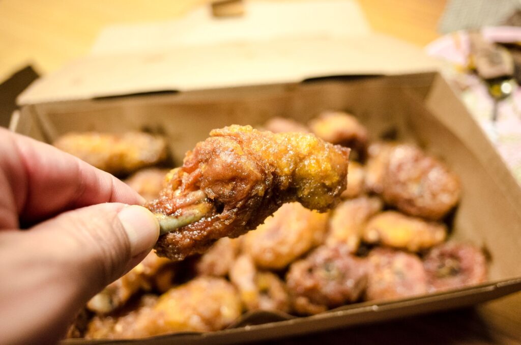 Gros plan d'un pilon de poulet frit croustillant tenu dans une main, prêt à être dégusté.
