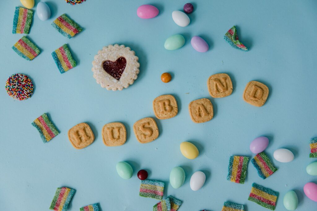 Disposition ludique de bonbons avec des biscuits formant 'Mari' sur un fond bleu pastel.