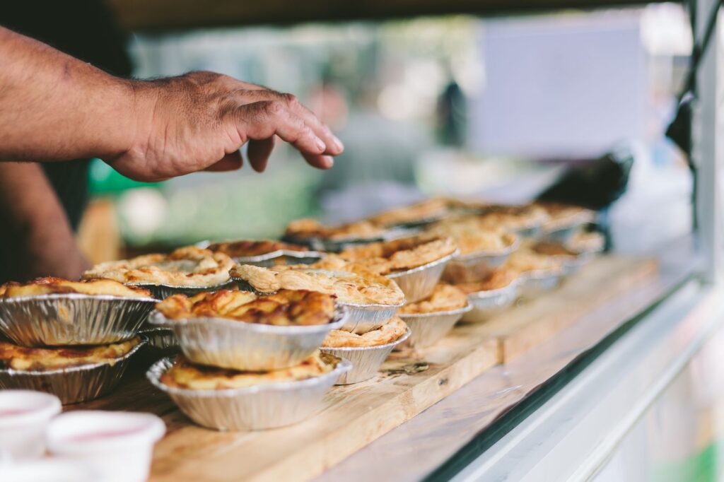 Main tendue vers de délicieuses tartes fraîchement cuites dans un marché en plein air à Rotorua.