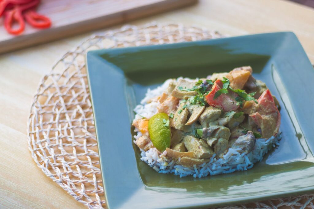 Gros plan sur un curry de poulet savoureux avec du riz servi dans une assiette verte, mettant en avant les ingrédients vibrants et frais.