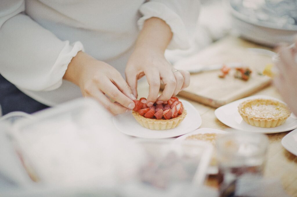Mains plaçant des fraises sur des tartes maison, mettant en valeur la préparation de plats avec des ingrédients frais.