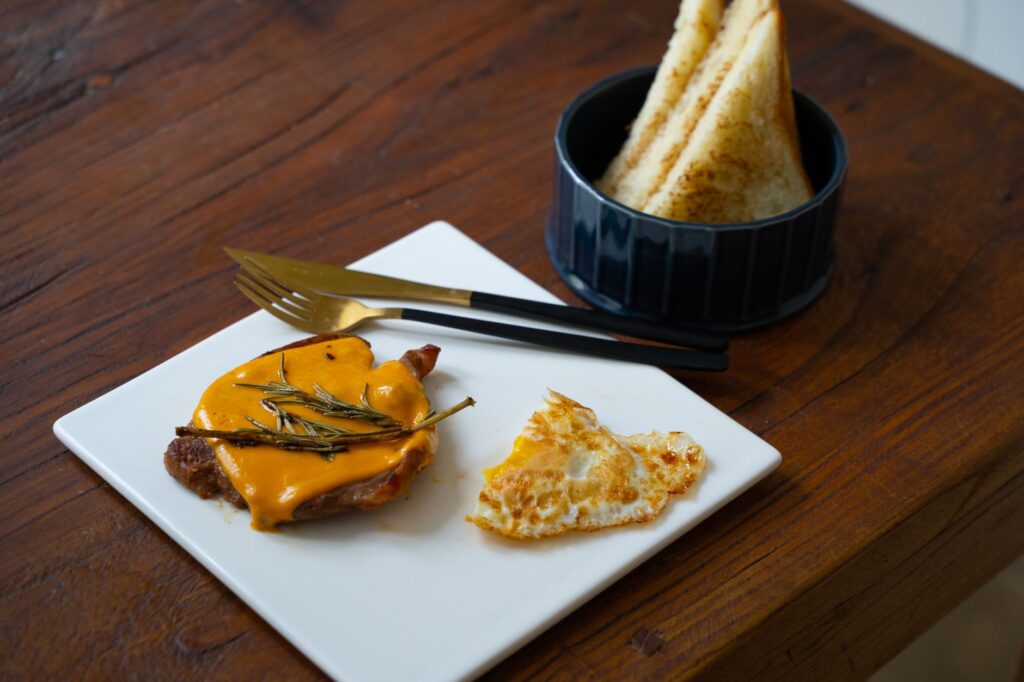 Un petit-déjeuner savoureux avec un œuf au plat, de la viande recouverte de fromage et du pain toasté sur une table en bois.