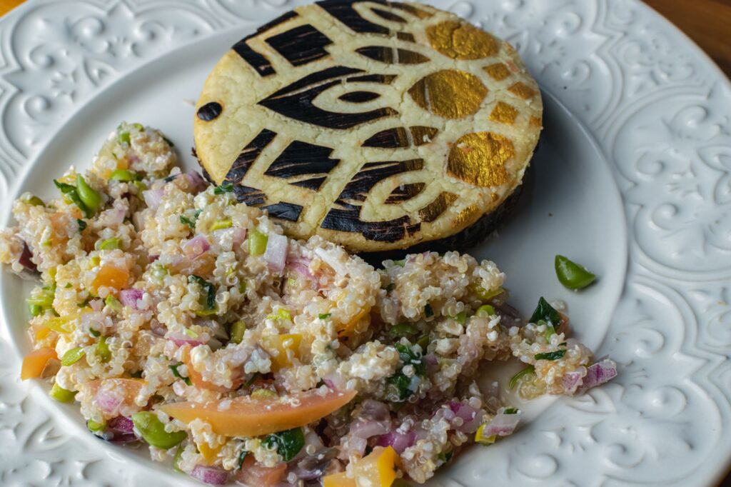 Un gros plan d'une tranche d'aubergine décorative accompagnée d'une salade de quinoa colorée sur une assiette ornée blanche.