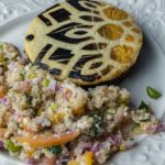 Un gros plan d'une tranche d'aubergine décorative accompagnée d'une salade de quinoa colorée sur une assiette ornée blanche.